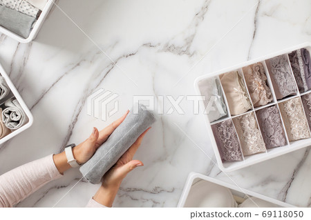 Woman hands neatly folding underwears and sorting in drawer organizers on white marble background. 69118050