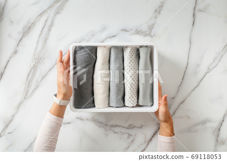Woman hands neatly folding underwears and sorting in drawer organizers on white marble background. 69118053