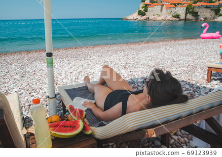 woman resting on sun lounger at rocky beach woman resting on sun lounger at rocky beach 69123939