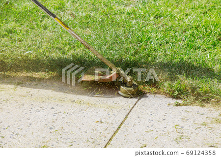 The gardener man mows the grass with a hand lawn The gardener man mows the grass with a hand lawn 69124358