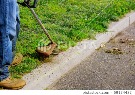 Worker in a gas mower in his hands, mowing grass Worker in a gas mower in his hands, mowing grass 69124482