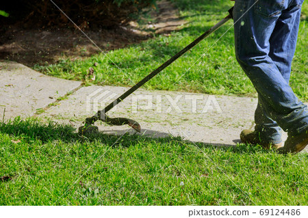 The gardener man mows the grass with a hand lawn The gardener man mows the grass with a hand lawn 69124486