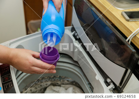 Woman hand pours liquid powder into the drum of Woman hand pours liquid powder into the drum of 69124658