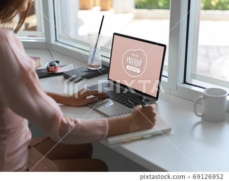 Young female typing on mock up laptop computer while writing her Young female typing on mock up laptop computer while writing her 69126952