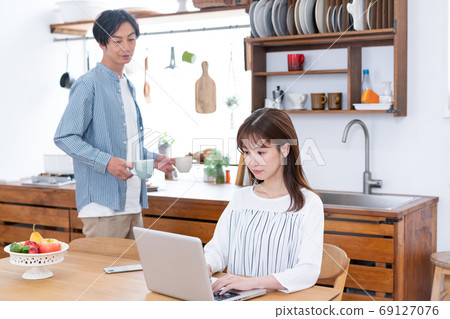 遠程辦公一名家庭主婦在飯廳裡的電腦上工作,還有一個溫柔的丈夫,他在煮茶 遠程辦公一名家庭主婦在飯廳裡的電腦上工作,還有一個溫柔的丈夫,他在煮茶 69127076