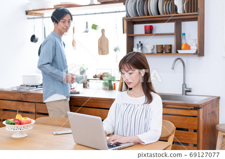 遠程辦公一名家庭主婦在飯廳裡的電腦上工作,還有一個溫柔的丈夫,他在煮茶 遠程辦公一名家庭主婦在飯廳裡的電腦上工作,還有一個溫柔的丈夫,他在煮茶 69127077