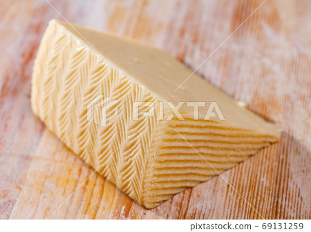 Slice of semi-soft cheese on a wooden table Slice of semi-soft cheese on a wooden table 69131259