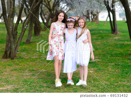 Three adorable girls in dresses hold hands in the garden, park. Three adorable girls in dresses hold hands in the garden, park. 69131432