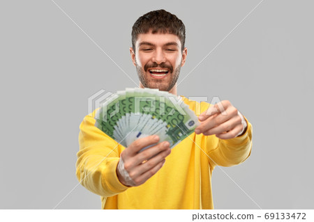 smiling young man in yellow sweatshirt with money 69133472