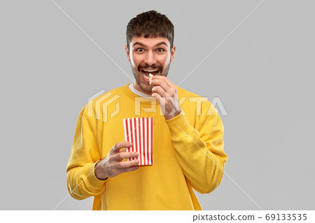 smiling man in yellow sweatshirt eating popcorn smiling man in yellow sweatshirt eating popcorn 69133535