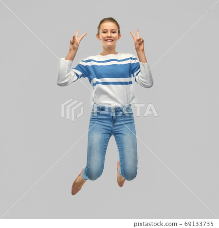 smiling teenage girl jumping and showing peace smiling teenage girl jumping and showing peace 69133735