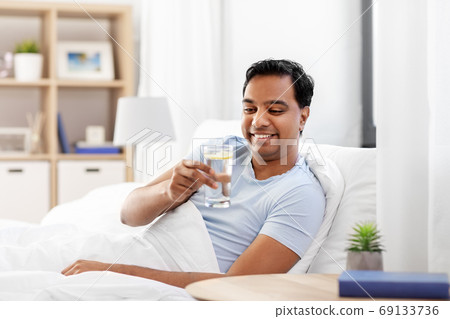 happy indian man drinking water lying in bed 69133736