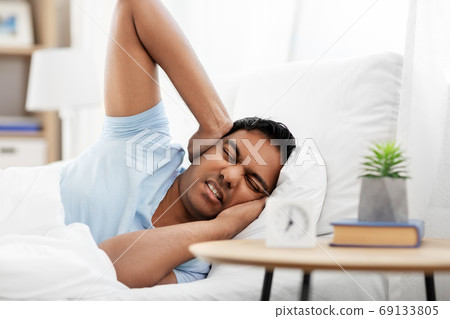 annoyed indian man with alarm clock lying in bed annoyed indian man with alarm clock lying in bed 69133805