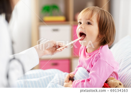 doctor checking sick girl's throat at home doctor checking sick girl's throat at home 69134163