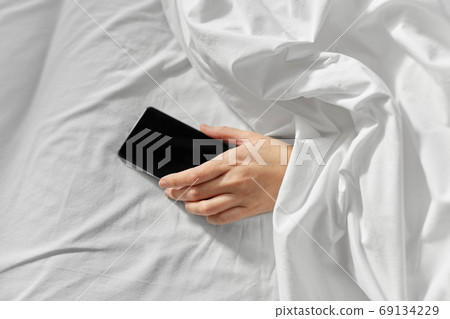 hand of woman lying in bed with smartphone hand of woman lying in bed with smartphone 69134229