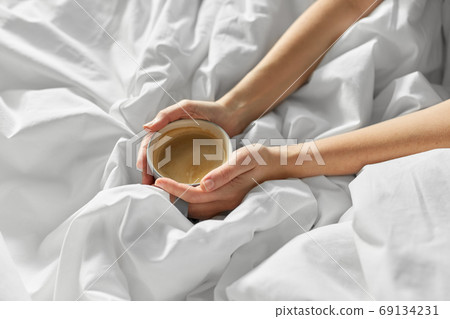 hands of woman with cup of coffee in bed hands of woman with cup of coffee in bed 69134231