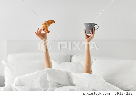 woman with coffee and croissant lying in bed woman with coffee and croissant lying in bed 69134232