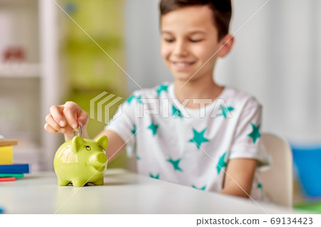 little boy putting coin into piggy bank at home 69134423