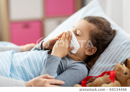 mother and ill little daughter blowing nose in bed 69134486