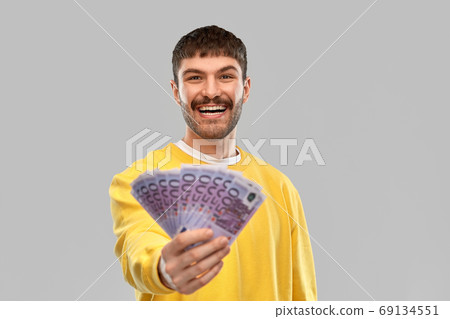 smiling young man in yellow sweatshirt with money 69134551
