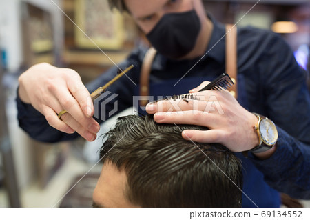 male hairdresser cutting hair at barbershop 69134552