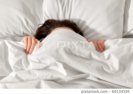 woman lying in bed under white blanket or duvet 69134595