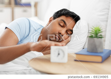 sleepy indian man with alarm clock lying in bed sleepy indian man with alarm clock lying in bed 69134905
