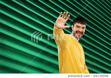 smiling young man in yellow sweatshirt waving hand smiling young man in yellow sweatshirt waving hand 69134946