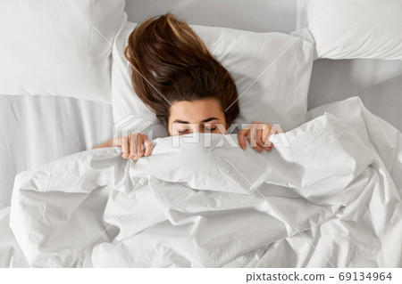 woman lying in bed under white blanket or duvet woman lying in bed under white blanket or duvet 69134964