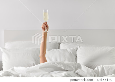 hand of woman lying in bed with champagne glass hand of woman lying in bed with champagne glass 69135120
