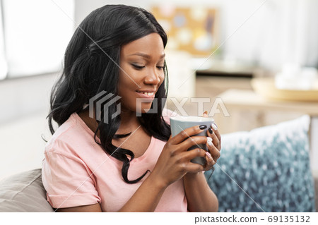 happy african woman drinking tea or coffee at home 69135132