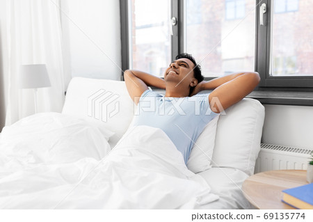 happy smiling indian man stretching in bed at home 69135774