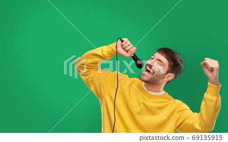 man in yellow sweatshirt with microphone singing man in yellow sweatshirt with microphone singing 69135915