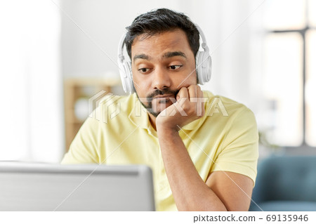bored man in headphones with laptop works at home bored man in headphones with laptop works at home 69135946