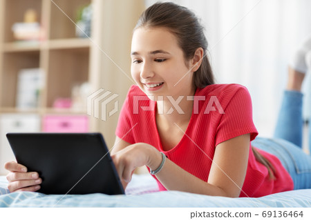 smiling girl with tablet pc lying on bed at home smiling girl with tablet pc lying on bed at home 69136464