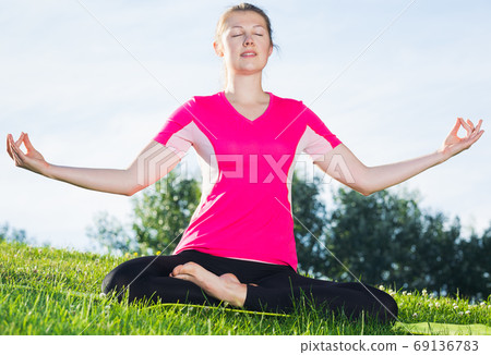 Female 26-32 years old in pink T-shirt is sitting and meditating Female 26-32 years old in pink T-shirt is sitting and meditating 69136783