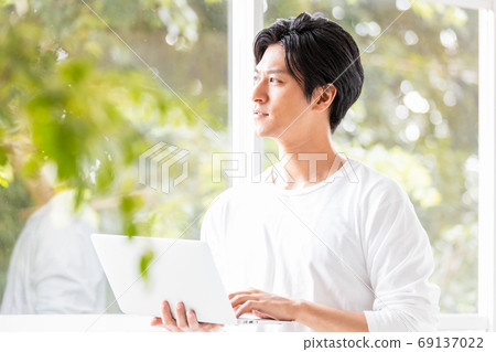 Young man standing on the windowsill with a laptop in hand 69137022