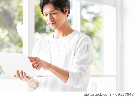Young man standing on the windowsill with a laptop in hand Young man standing on the windowsill with a laptop in hand 69137048