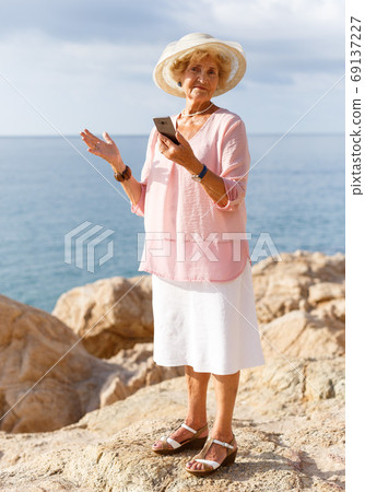 Elderly woman using phone at seaside Elderly woman using phone at seaside 69137227