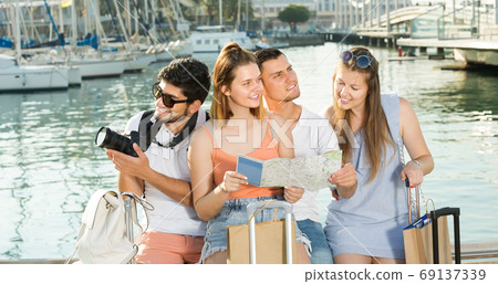 Four traveling young people searching for direction using paper map on waterfront in town Four traveling young people searching for direction using paper map on waterfront in town 69137339