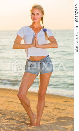 Adult woman in white T-shirt is staying and practicing asana Adult woman in white T-shirt is staying and practicing asana 69137629
