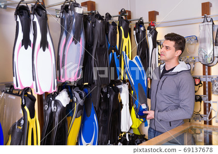 Man is standing with modern diving flippers in the store. Man is standing with modern diving flippers in the store. 69137678
