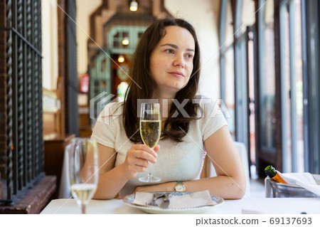 Positive woman holding glass of white wine in restaurant Positive woman holding glass of white wine in restaurant 69137693