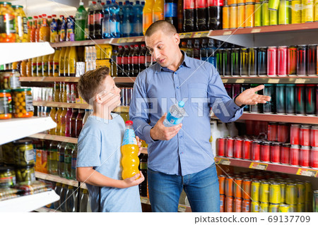 Smiling father friendly discussing with preteen boy while choosing beverages in food store Smiling father friendly discussing with preteen boy while choosing beverages in food store 69137709