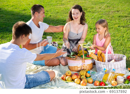 Happy parents with two kids having picnic together on green meadow in park Happy parents with two kids having picnic together on green meadow in park 69137892