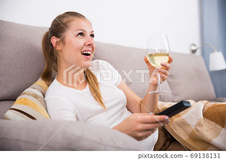 Young woman is sitting with white wine and watching TV Young woman is sitting with white wine and watching TV 69138131