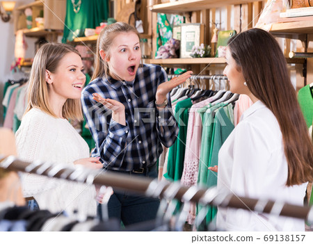 Three young women friends talking in fashion clothes shop Three young women friends talking in fashion clothes shop 69138157