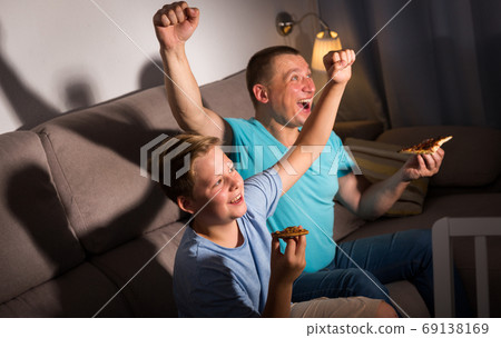 Smiling man is watching TV and cheering for football team with his son Smiling man is watching TV and cheering for football team with his son 69138169