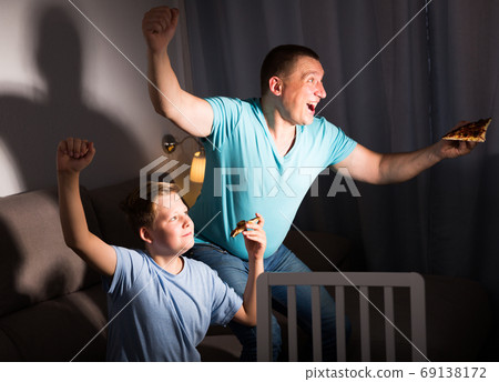 Smiling man is watching TV and cheering for football team with his son Smiling man is watching TV and cheering for football team with his son 69138172