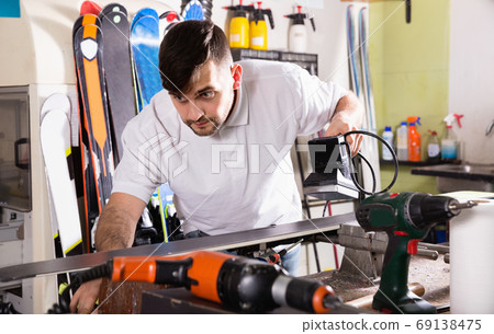 Confident master of ski service professionally performing sharpening of edges on skis 69138475